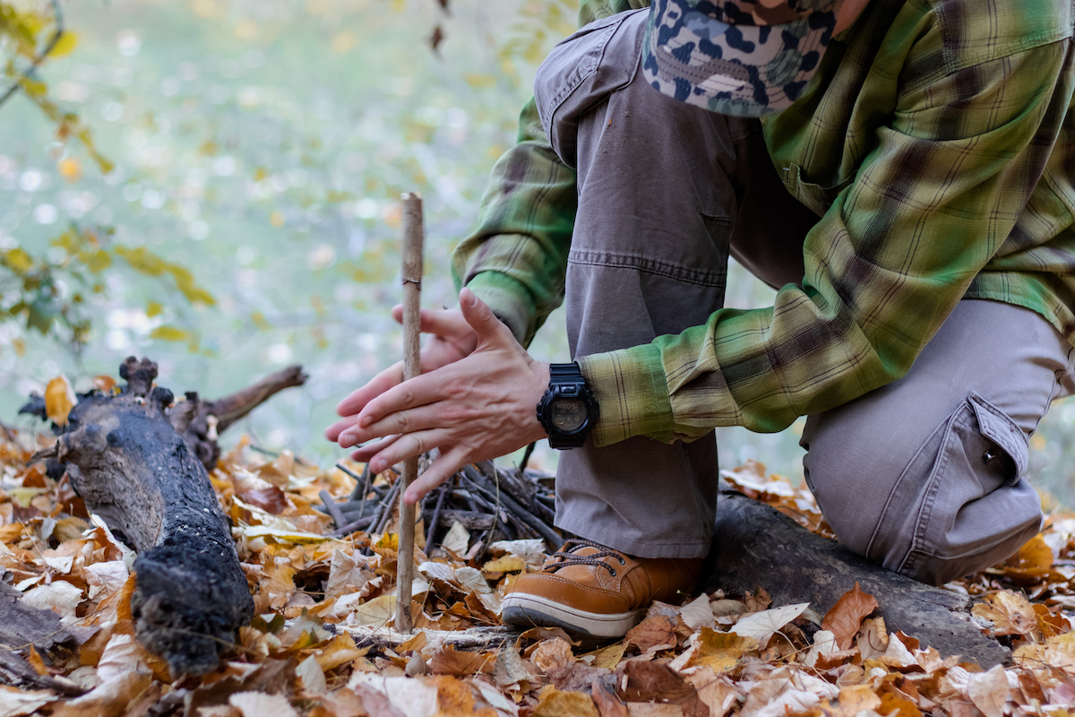 Learning how to make fire is an essential survival skill, here, a person is using primitive means to start a fire in the woods.